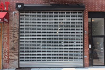 Storefront open grid security gate aka grille. Most of the area covered by the gate is visible from the sidewalk.